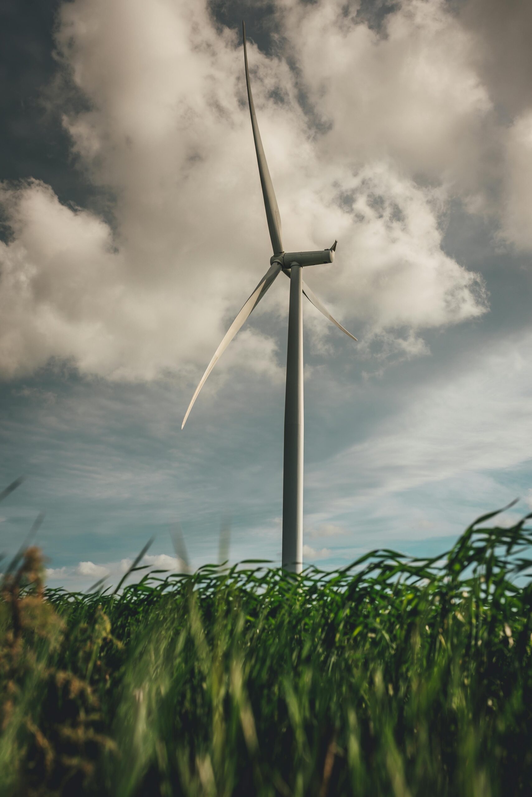 A wind turbine stands tall amidst green grass under a dramatic cloudy sky, symbolizing renewable energy.